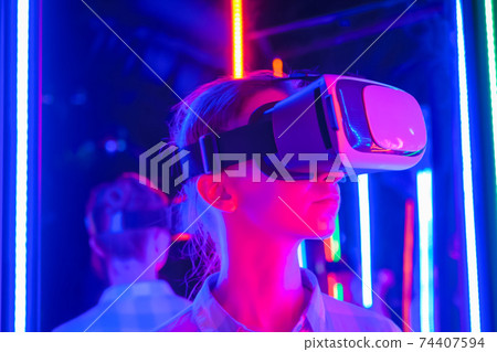 Young woman using virtual reality headset at dark interactive VR exhibition Young woman using virtual reality headset at dark interactive VR exhibition 74407594