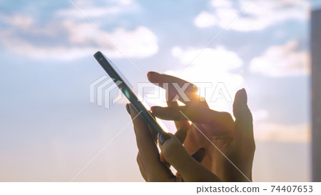 Woman hand using smartphone against sunshine, sun lens flare: close up side view Woman hand using smartphone against sunshine, sun lens flare: close up side view 74407653