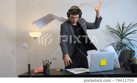 A young specialist listens to music and vigorously dances in the workplace. 74411724