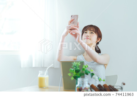 一個年輕的女人在家裡採取與她的智能手機的自拍照 一個年輕的女人在家裡採取與她的智能手機的自拍照 74411963