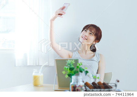 一個年輕的女人在家裡採取與她的智能手機的自拍照 一個年輕的女人在家裡採取與她的智能手機的自拍照 74411964