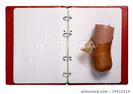 A piece of cooked sausage on a sheet of an open squared notebook A piece of cooked sausage on a sheet of an open squared notebook 74412514