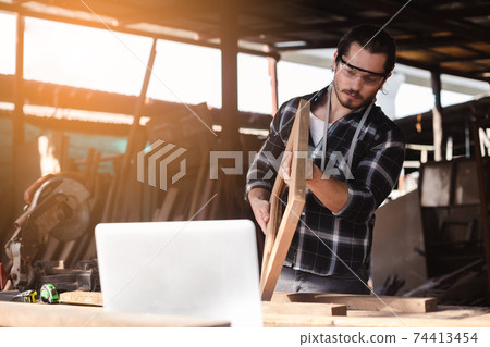 young carpenter man working perpendicular wooden selection at work table in wood factory. young carpenter man working perpendicular wooden selection at work table in wood factory. 74413454