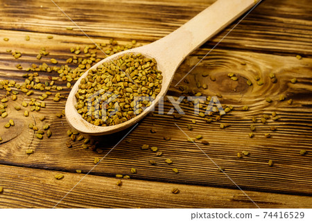 Fenugreek seeds in wooden spoon on wooden table 74416529