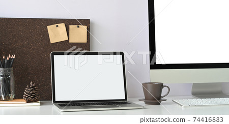 A white blank screen laptop is putting on a white working desk surrounded by office equipment. 74416883