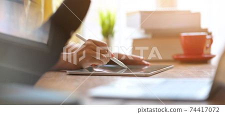 Businesswomen are working together by using a computer laptop and tablet at the wooden working desk. Businesswomen are working together by using a computer laptop and tablet at the wooden working desk. 74417072