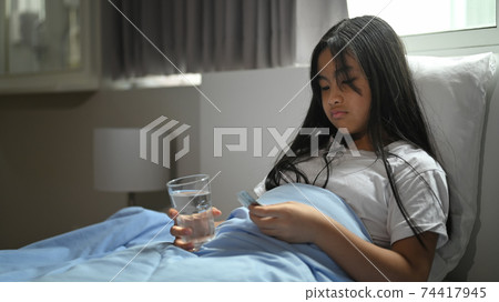 Sick little girl covered in a blanket is lying on the bed and taking a pill. Sick little girl covered in a blanket is lying on the bed and taking a pill. 74417945