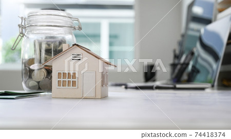 Home model and glass jars with coins putting on white table..Planning savings money to buy a home or Property Investment concept. Home model and glass jars with coins putting on white table..Planning savings money to buy a home or Property Investment concept. 74418374