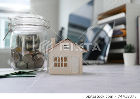 Close up view of glass jars with coins and house model on table. Planning savings money to buy a home, Real estate or property investment. 74418375