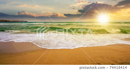 sea tide on a cloudy sunrise. green waves crashing golden sandy beach in morning light. storm weather approaching. summer holiday concept sea tide on a cloudy sunrise. green waves crashing golden sandy beach in morning light. storm weather approaching. summer holiday concept 74418414