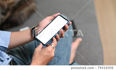 Cropped shot of young man sitting on comfortable sofa at home and using mobile phone. 74418509