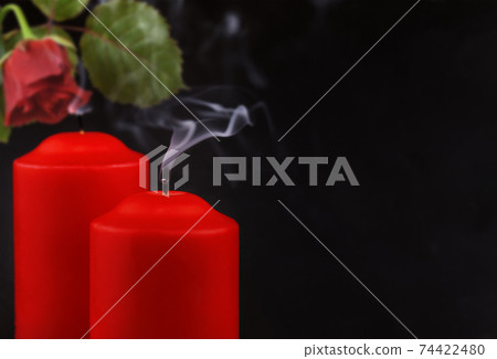 Two red extinguished candles with white smoke and withered rose flower on black 74422480