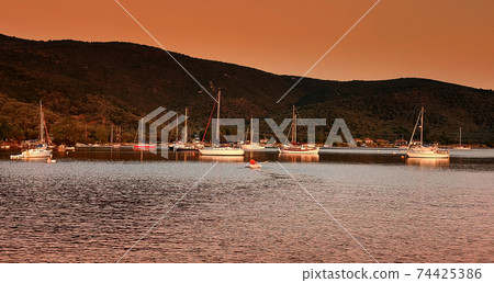 Sailboats anchored in a beautilful bay at sunset Sailboats anchored in a beautilful bay at sunset 74425386