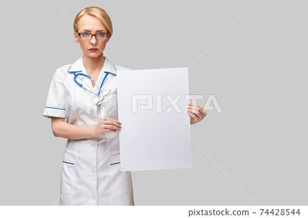 Female doctor holding a blank banner sign standing over grey background 74428544