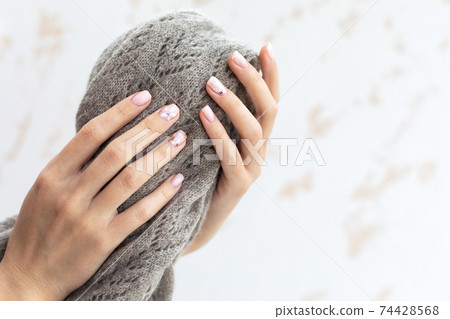 Pastel beige manicure on the light background. Manicured nails and soft hands skin with copy space. Woman's hands on warm scarf. 74428568