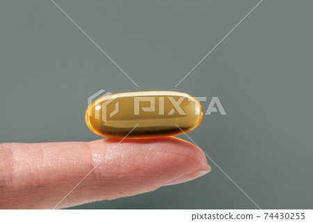 Female hand holding a big yellow capsule of nutritional supplement. Food supplement, vitamin D, omega, vitamin C. Female hand holding a big yellow capsule of nutritional supplement. Food supplement, vitamin D, omega, vitamin C. 74430255