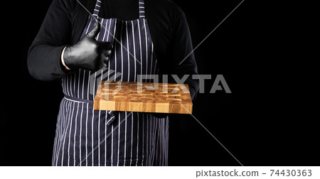male chef in a striped blue apron holds in his hand a rectangular wooden kitchen chopping board 74430363