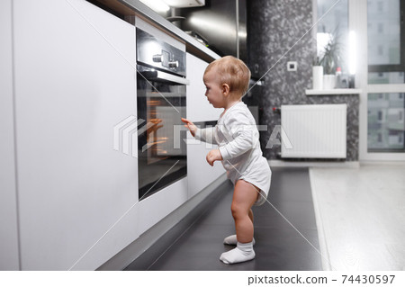 Infant baby boy near oven in home kitchen. Infant baby boy near oven in home kitchen. 74430597