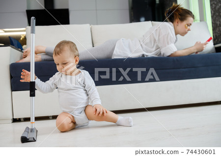 Baby boy play with mop, while mother surfing in your smartphone lying on couch 74430601