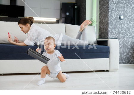 Baby boy play with mop, while mother surfing in your smartphone lying on couch Baby boy play with mop, while mother surfing in your smartphone lying on couch 74430612