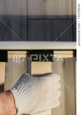 Male worker's hand in glove assembling bed, connecting slats to bed frame 74430684