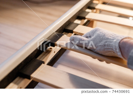 Male worker's hand in glove assembling bed, connecting slats to bed frame 74430691