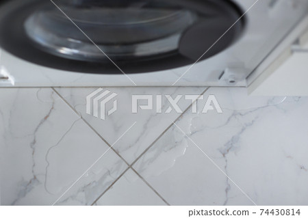 Spilled water leaked from washing machine built into the kitchen furniture. Spilled water on the tiled floor, flooding. 74430814