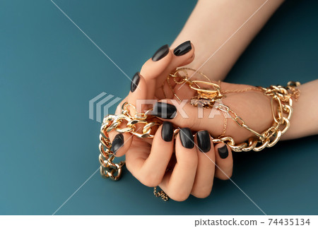 Female hands with trendy dark nail design with gold bracelets on aqua background. Luxury concept. 74435134