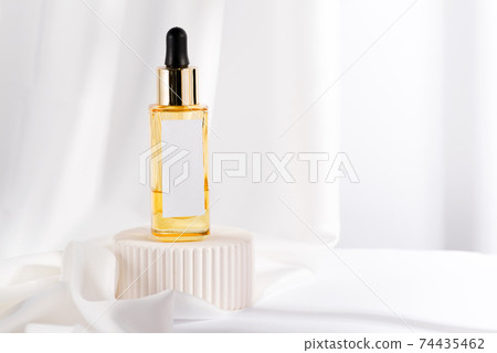 Yellow serum essence in glass bottle on white stand background. Isolated skincare oil Yellow serum essence in glass bottle on white stand background. Isolated skincare oil 74435462