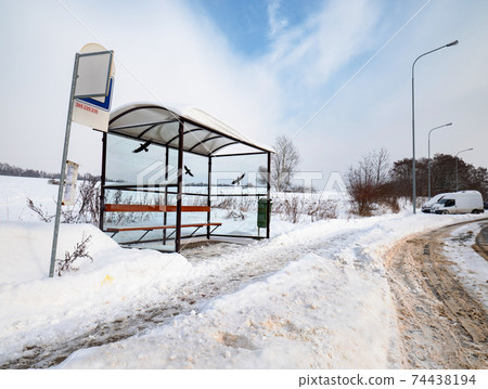Empty suburban bus stop covered with snow in winter. Slipery pavement with sand and salt mix treatments. Empty suburban bus stop covered with snow in winter. Slipery pavement with sand and salt mix treatments. 74438194