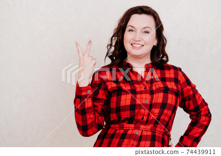 two. Attractive brunette woman in red checkered dress on white shows fingers.  74439911