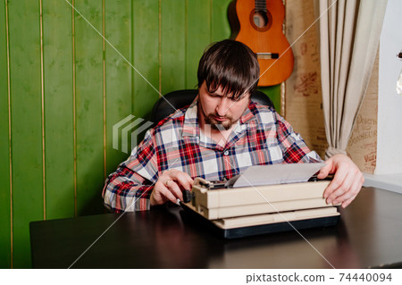 a man in plaid pajamas types on a typewriter at night in his home office. a man in plaid pajamas types on a typewriter at night in his home office. 74440094