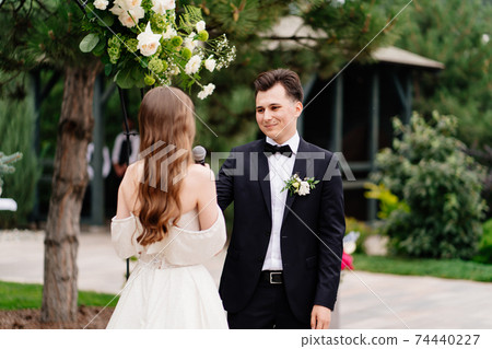 wedding ceremony in arch of living flowers. the groom listens to the bride's vow wedding ceremony in arch of living flowers. the groom listens to the bride's vow 74440227