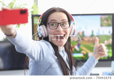 Joyful woman gamer shoots video on smartphone on background of computer game Joyful woman gamer shoots video on smartphone on background of computer game 74441674