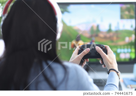 Female gamer sits with her back holding game joystick and plays game on the computer 74441675