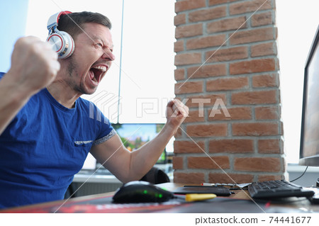 Male gamer in headphones emotionally reacts to winning game Male gamer in headphones emotionally reacts to winning game 74441677