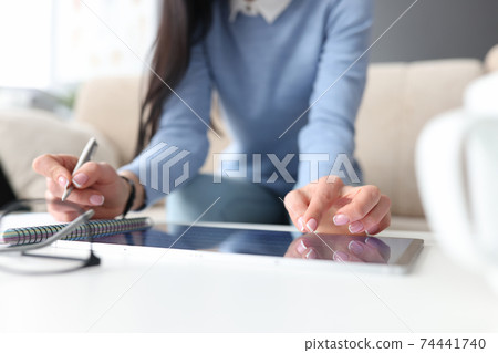 Female hand on tablet with second hand makes notes with pen in notebook Female hand on tablet with second hand makes notes with pen in notebook 74441740