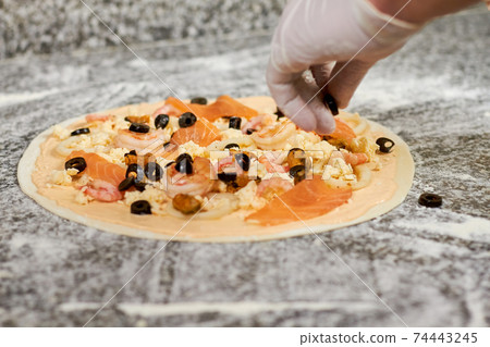 Adding black olives to pizza. Adding black olives to pizza. 74443245