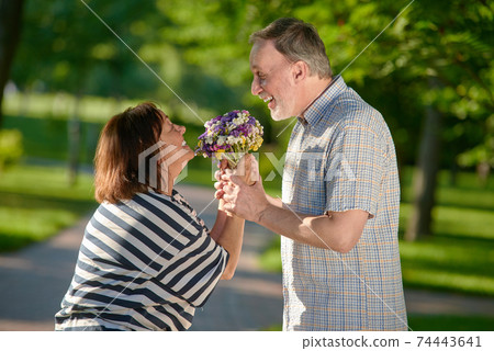 Happy mature couple holding flowers outdoors. Happy mature couple holding flowers outdoors. 74443641