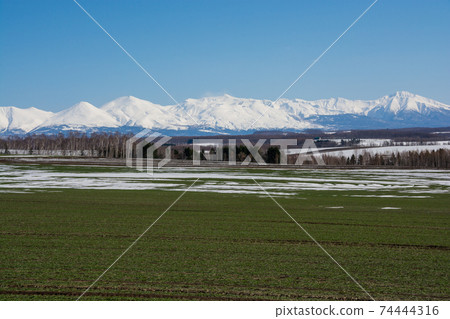 Green fields and snowy mountains with residual snow on a clear spring day Tokachidake mountain range Green fields and snowy mountains with residual snow on a clear spring day Tokachidake mountain range 74444316
