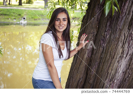 pretty young woman smiling cheerful in green park at tree on summer sunny day, lifestyle people concept 74444769