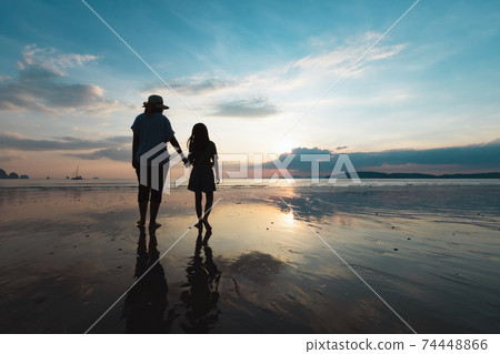 Silhouette of asian mother and daughter holding hand and walking on the beach together at the sunset time with beautiful sea and sky. Family enjoy with nature concept. Silhouette of asian mother and daughter holding hand and walking on the beach together at the sunset time with beautiful sea and sky. Family enjoy with nature concept. 74448866