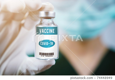 Doctor wear face mask protective gloves holding coronavirus vaccine in glass bottle. Doctor wear face mask protective gloves holding coronavirus vaccine in glass bottle. 74448949