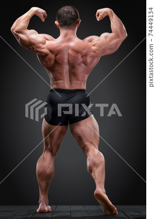 Classic bodybuilder showing his back muscles in tension against a dark grey background 74449134