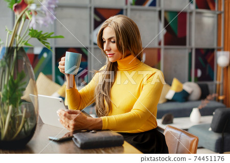 Portrait of a beautiful businesswoman enjoying coffee while working on a tablet while having breakfast at home. Business portrait, Business online, work at home Portrait of a beautiful businesswoman enjoying coffee while working on a tablet while having breakfast at home. Business portrait, Business online, work at home 74451176