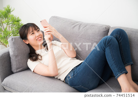 A woman lying on the sofa and operating a smartphone 74451514