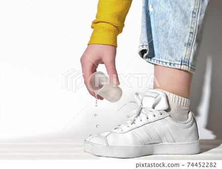 female hand pouring water on a white sneakers. female hand pouring water on a white sneakers. 74452282