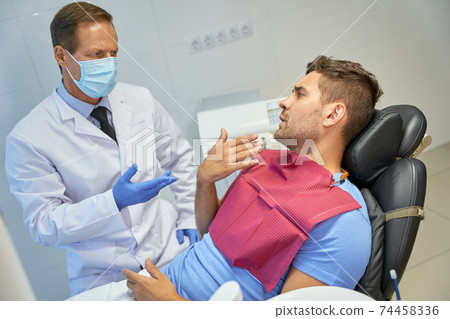 Troubled dental specialist explaining something to his male patient 74458336
