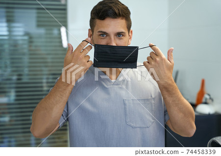 Handsome doctor demonstrating a way to put mask on 74458339