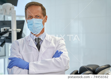 Qualified dentist in a mask standing with his arms crossed 74458382